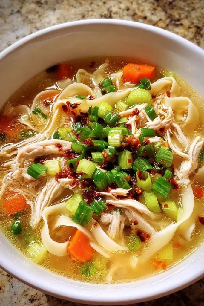 Bowl of classic ginger garlic chicken noodle soup garnished with herbs